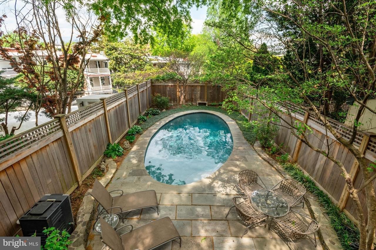 A lush green backyard oasis with stone patio, outdoor furniture, and teal, oval-shaped swimming pool